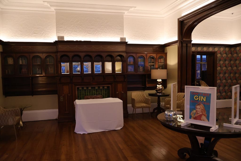 The Morning Room at Pendrell Hall featuring dark wood paneling, an ornate fireplace, and elegant seating, with a Wards Photo Booths "Especially for Sober You" sign on a table in the foreground.