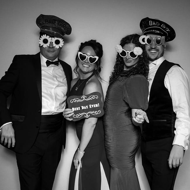 Group of guests in formal attire posing for a black and white glam photo booth with "Bad Boy" and "Bad Girl" hats in the West Midlands.