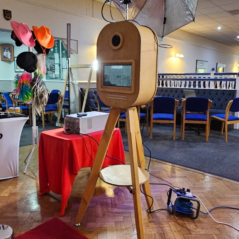 Full setup of a vintage wooden pod photo booth with a prop stand and red carpet at a West Midlands event venue.